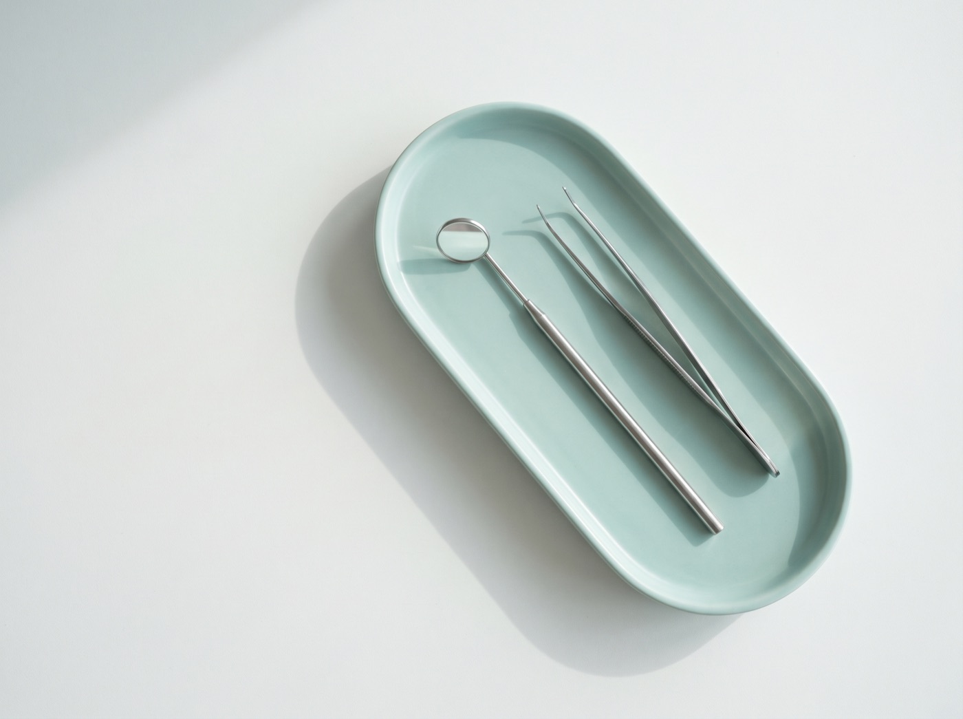 A dental mirror and tweezers on a pale teal tray